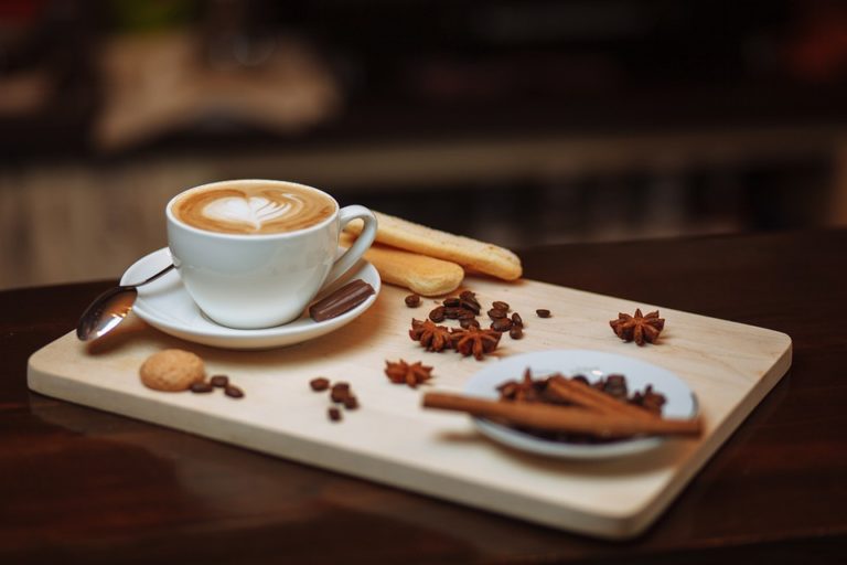 A cup of black coffee with a visible crema on a wooden surface next to scattered coffee beans