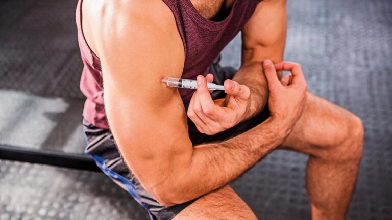 Several vials and pills labeled as anabolic steroids arranged on a reflective surface